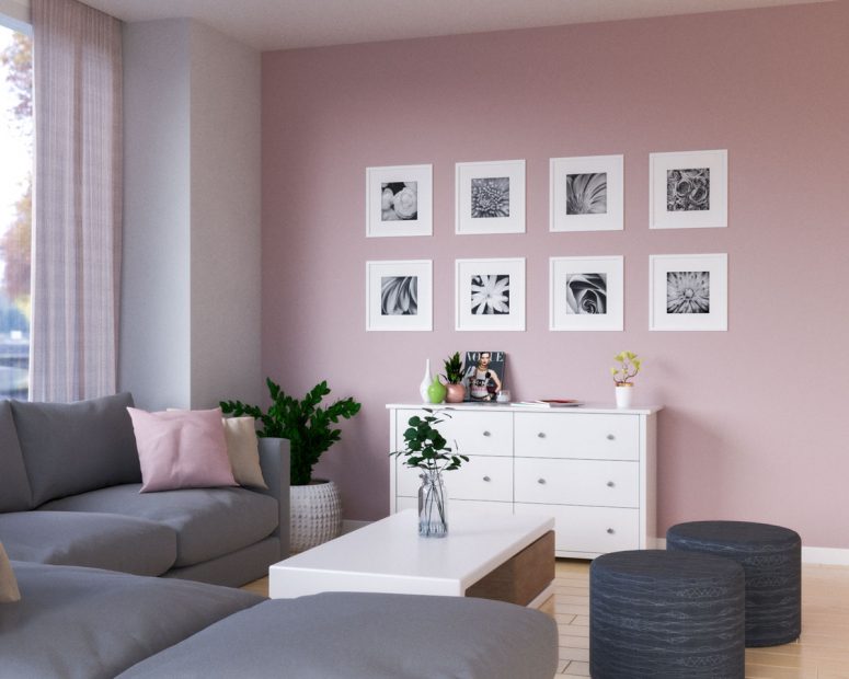 a stylish modern living room with a pale pink accent wall and a grid gallery wall, a white sideboard, a grey sectional, a low white coffee table