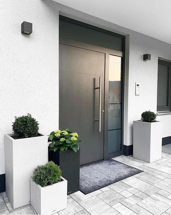 a stylish modern porch with a black metal door, grey and black tall square planters with greenery