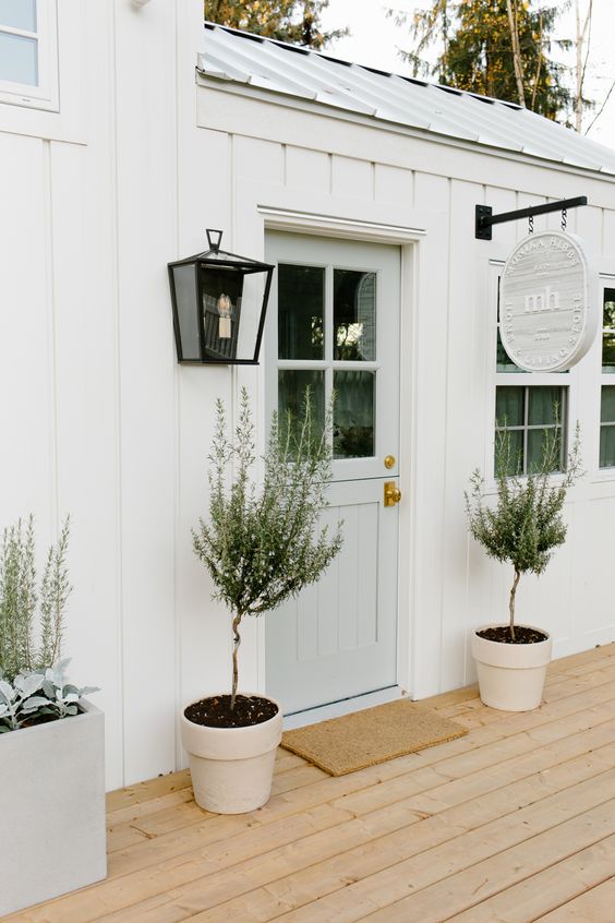 a stylish neutral porch with an aqua door, potted trees, a black lantern attached to the wall and a hanging sign