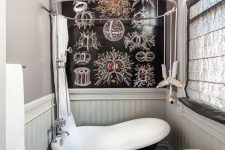 a tiny yet fancy bathroom with a mosaic tile floor, a black painted wall, a black vintage soak tub and a brass chandelier