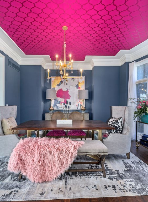 a unique dining room with navy walls and a hot pink ceiling, a wooden table and upholstered chairs, a gold chandelier