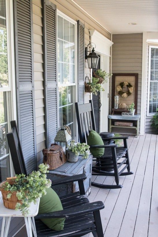 a vintage farmhouse porch with black rockers, a grey chest, potted greenery, a basket, a console and a wreath of wheat
