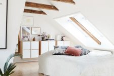 a welcoming attic bedroom with wooden beams, floating dressers and a bed by the skylight, a bright rug and pillows and a potted plant