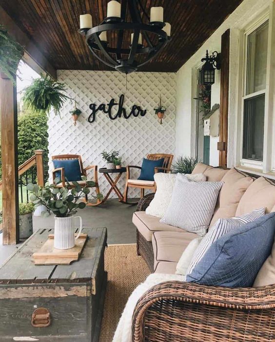 a welcoming farmhouse porch with a large wicker sofa, a chest coffee table, rattan rockers, potted greenery and a vintage chandelier