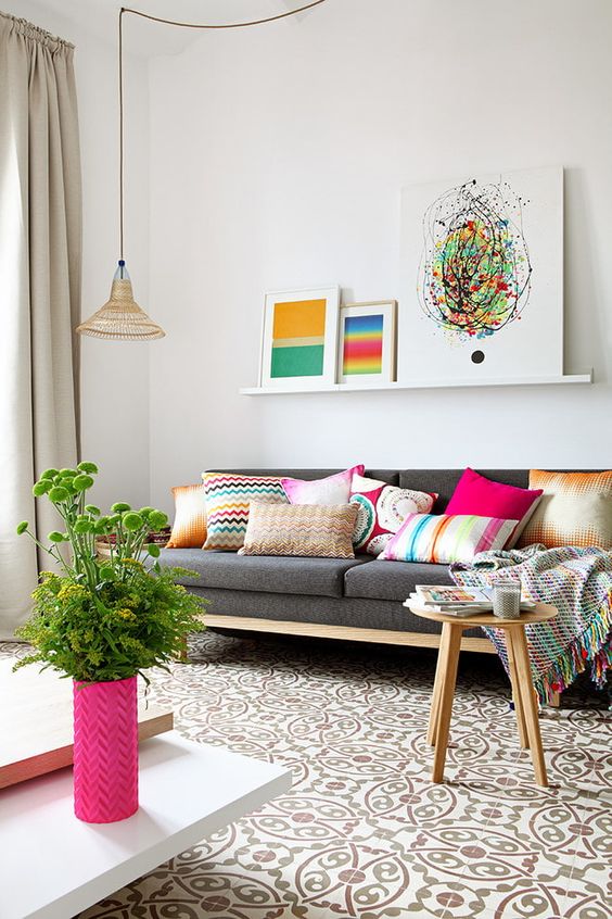 a welcoming living room with a grey sofa, a ledge gallery wall with bright artworks, hot pink accessories and a bold mosaic tile floor