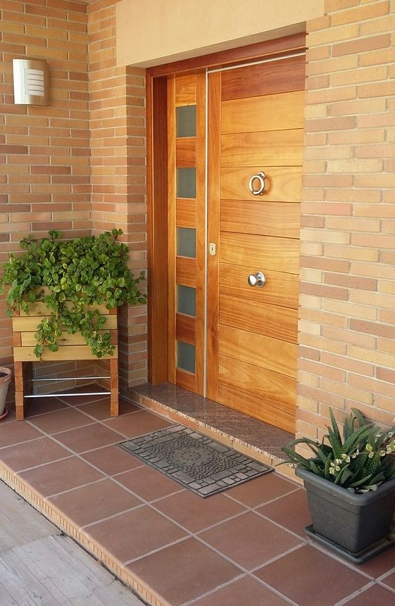 a wooden planter on tall legs and a small grey planter with different types of greenery to frame the door