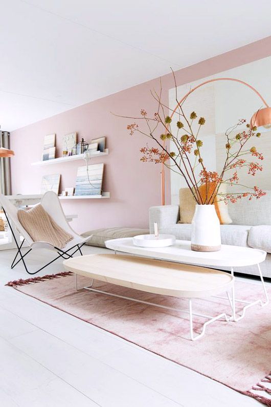 an airy and dreamy living room with a light pink accent wall, chic Scandinavian furniture, low coffee tables, a cool artwork and ledge gallery walls