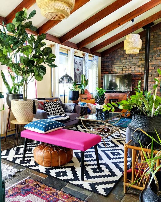 an eclectic attic space with an extended brick wall, wooden beams on the ceiling, a sofa, a hot pink bench and potted plants is cool