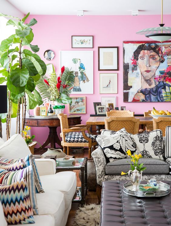 an eclectic space with a hot pink accent wall and a gallery wall, quirky and mismatching furniture, lots of potted plants and blooms and printed pillows