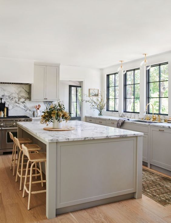 an inspiring dove grey modern country kitchen with shaker style cabients, white marble countertops, gold touches and rattan stools