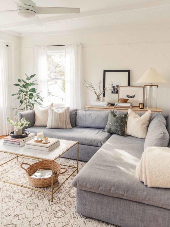 an organic modern country living room with a grey sectional, a coffee table, a basket, some plants and cool pillows