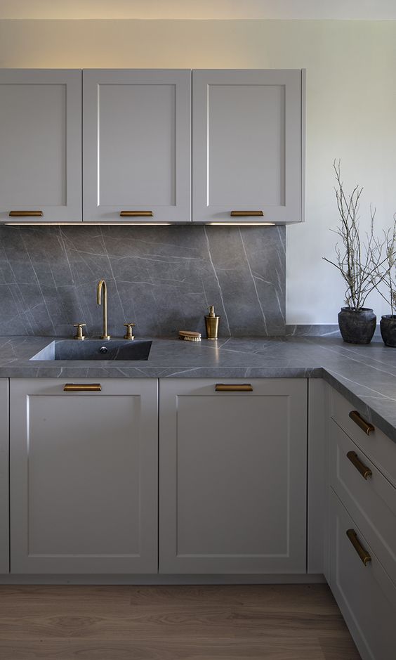 a modern grey kitchen with a grey marble backsplash and countertops, brass fixtures is a very chic and bold solution