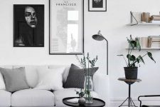 16 a laconic living room in Scandi style, with a white sofa, open shelves, black tables and a chair, black and white gallery wall