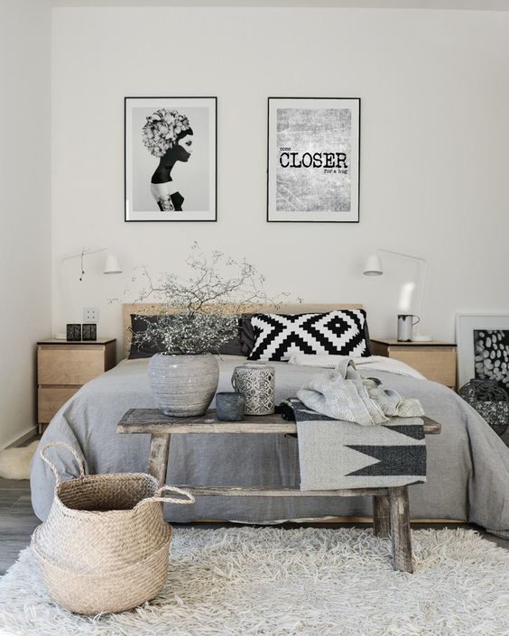 a Scandinavian bedroom with light stained furniture, printed bedding, a bench and a basket for storage plus a couple of artworks