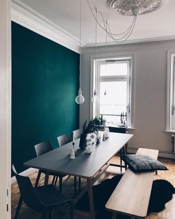 a Scandinavian dining space with a bold green accent wall, a chic table with a black tabletop, matching grey chairs and pendant bulbs