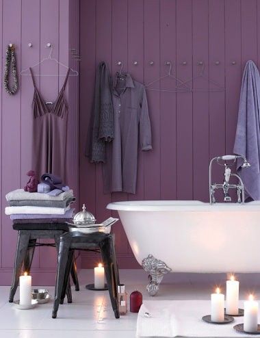 a beautiful bathroom with a purple planked accent wall, a refined vintage bathtub, black metal stools and candles around