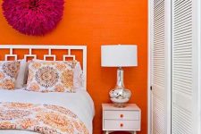 a bold bedroom with an orange wallpaper accent wall, white mid-century modern furniture, a fuchsia decoration and a wardrobe with shutter doors