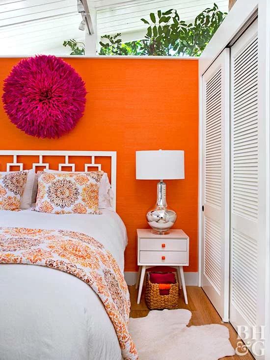 a bold bedroom with an orange wallpaper accent wall, white mid-century modern furniture, a fuchsia decoration and a wardrobe with shutter doors