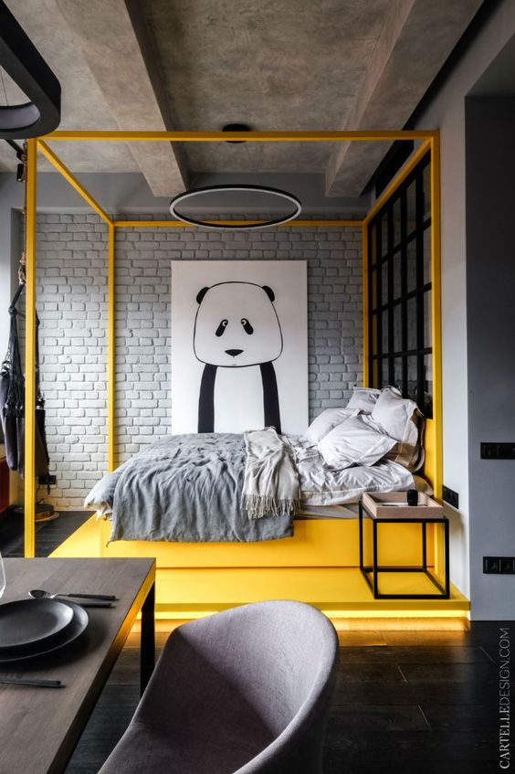 a bold contemporary bedroom with a yellow canopy bed on a yellow lit up platform, grey bedding, a round chandelier and a statement wall art