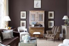 a bold eclectic living room with a deep purple accent wall and a matching sofa, a gallery wall, a refined chandelier, a mirror coffee table and a printed chair