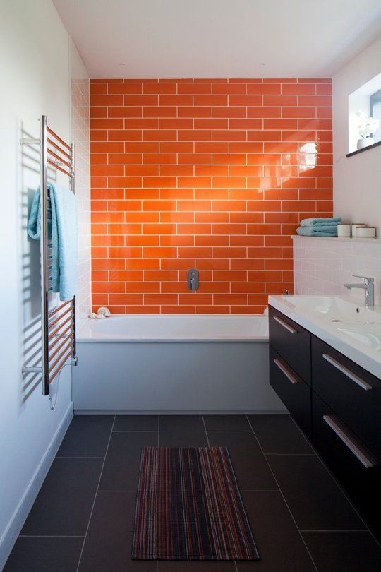 a bold modern bathroom with an orange tile accent wall and large scale tiles on the floor, a dark floating vanity and some windows for more light