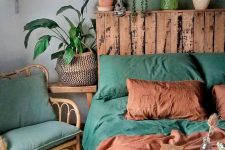 a bright boho bedroom done in green and rust shades, with lots of potted plants, a rattan chair and a bed with a pallet headboard