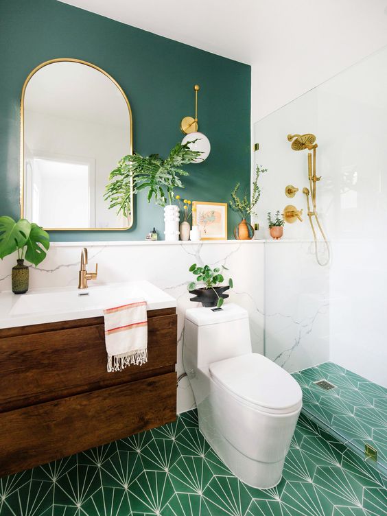 a chic modern bathroom with a green accent wall and a green mosaic tile floor, a stained vanity, an arched mirror and potted plants