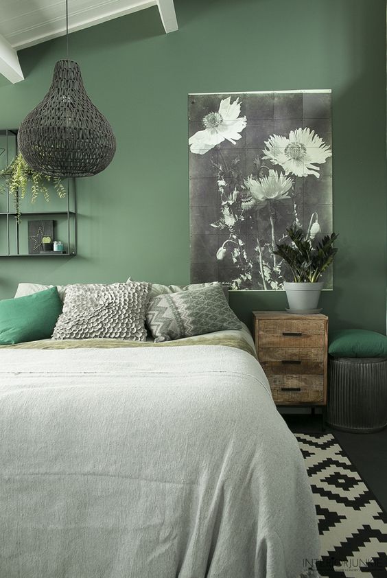 a chic organic bedroom with a green accent wall, a bed, a shabby chic nightstand, a woven pendant lamp and a chic floral artwork