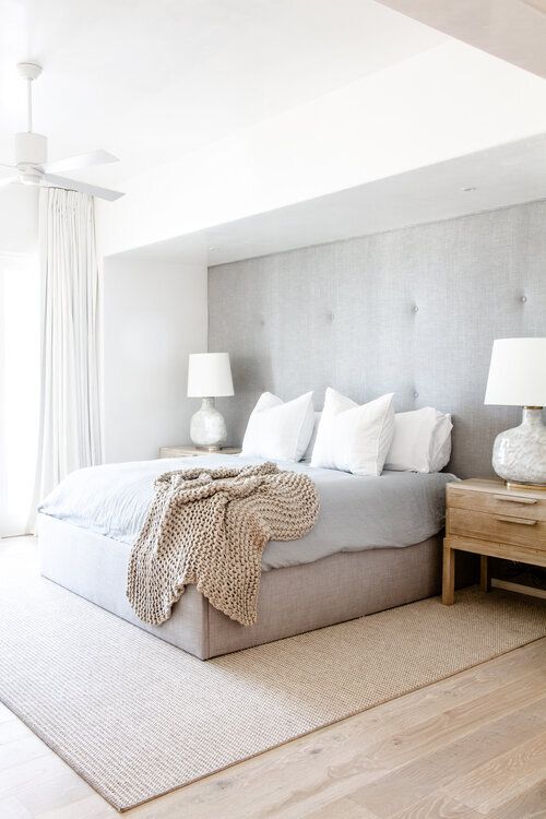 a clean neutral contemporary bedroom with a grey upholstered wall and an upholstered bed that matches, neutral textiles and a large rug