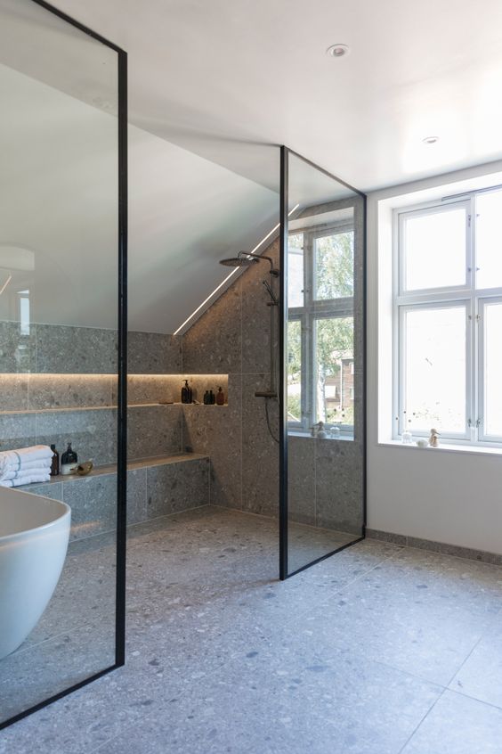 a contemporary attic bathroom clad with grey terrazzo tiles, a shower space, a lit up niche for storage, some windows
