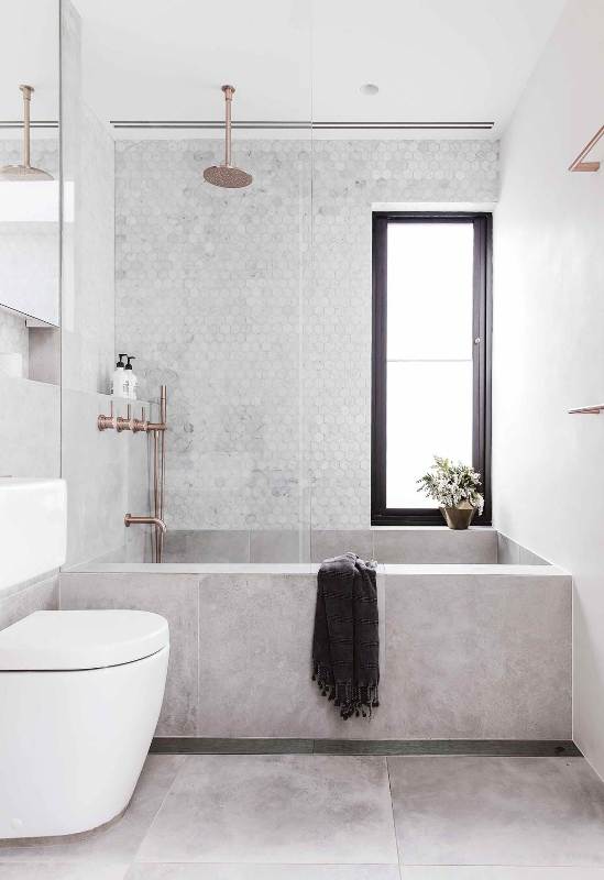 a contemporary bathroom clad with concrete and marble hex tiles, a tub clad with concrete tiles, white appliances and cropped fixtures