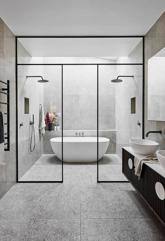 a contemporary bathroom clad with grey terrazzo tiles, a skylight over the tub, a black vanity and black framing, black fixtures
