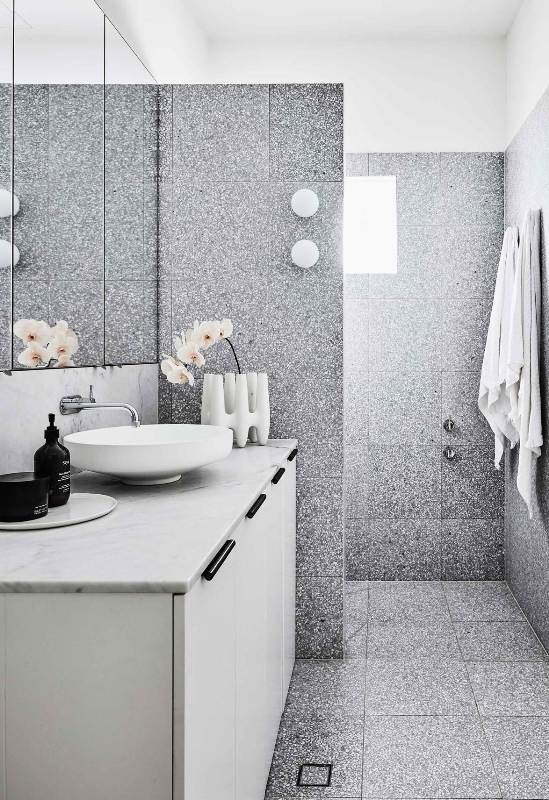 a contemporary bathroom clad with grey terrazzo tiles, with a white vanity, a marble countertop, a round sink, a cool vase and orchids