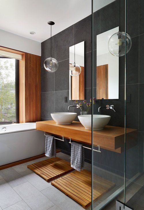 a contemporary bathroom clad with grey tiles of various shades, a bathtub, a floating vanity, wooden mats and accents