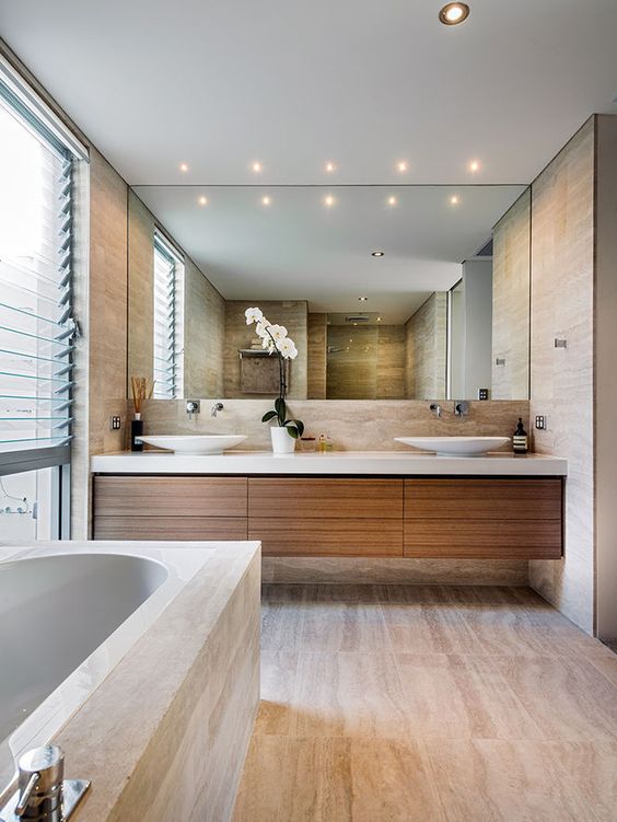 a contemporary bathroom clad with neutral stone-imitating tiles, a floating vanity, a large mirror, a glazed wall with shades
