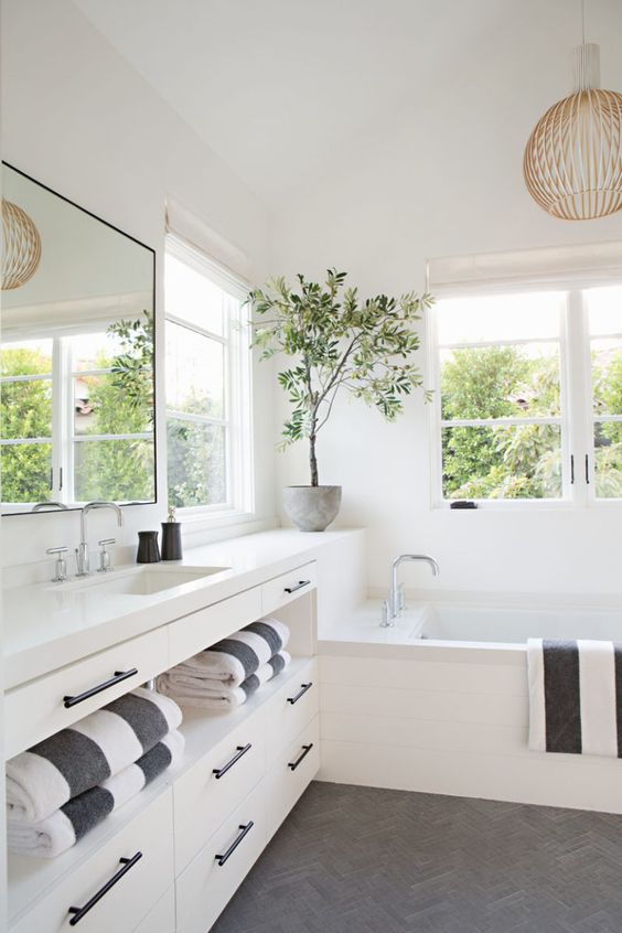 a contemporary bathroom done in white, with a grey chevron floor, a large vanity with plenty of storage, windows and a large mirror