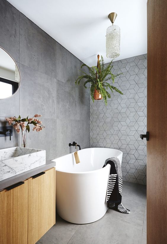 a contemporary bathroom with large scale concrete and geometric tiles, an oval tub, a floating vanity and a white marble sink plus greenery