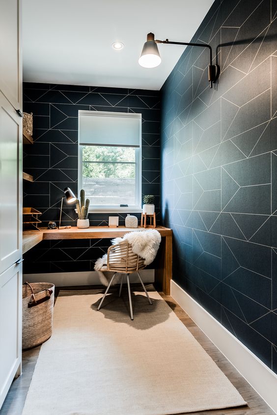 a contemporary home office with black geo wallpaper walls, a corner desk and a rattan chair plus modern lamps