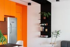 a contemporary open layout with a black and white accent and a whole orange accent wall with orange cabinets and a door is very bold