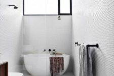 a dove grey bathroom with penny and large scale tiles, a wooden ceiling, an oval tub and black fixtures is very stylish