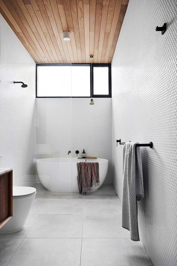 a dove grey bathroom with penny and large scale tiles, a wooden ceiling, an oval tub and black fixtures is very stylish