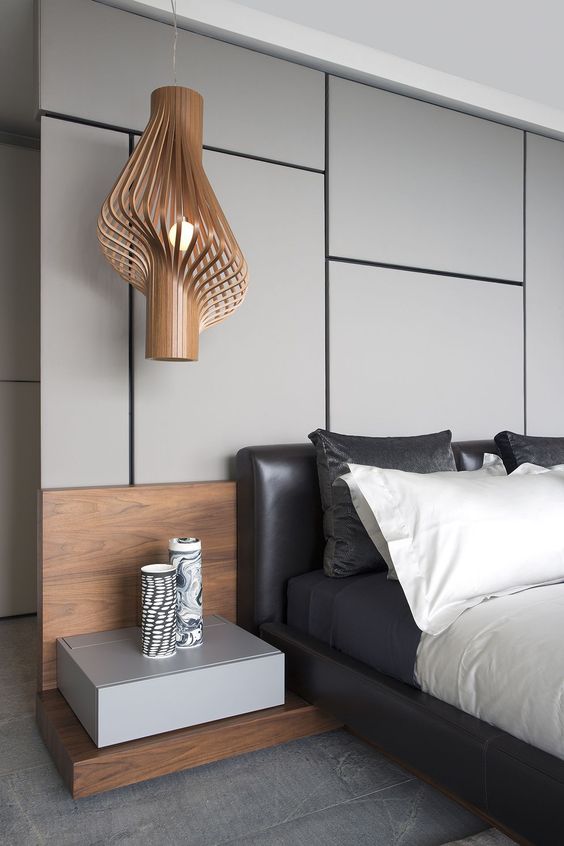 a gorgeous contemporary bedroom with a grey panel accent wall, a black leather bed, contrasting bedding, a floating nightstand and a jaw-dropping pendant lamp
