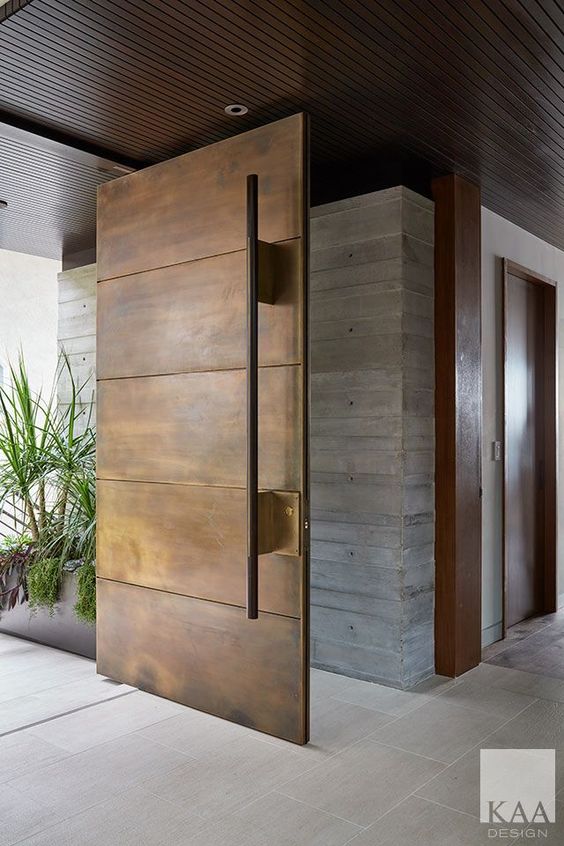 a heavy aged metal pivot door with a large handle is a bold idea for a contemporary space and can be rocked in any modern entrance