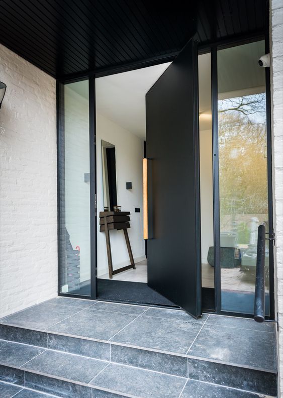 a heavy black metal pivot door with a long light stained handle is a cool idea for making and statement with style