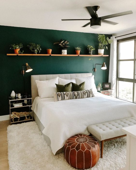 a lovely mid-century modern bedroom with a green accent wall, a creamy upholstered bed and a bench, a shelf with potted greenery