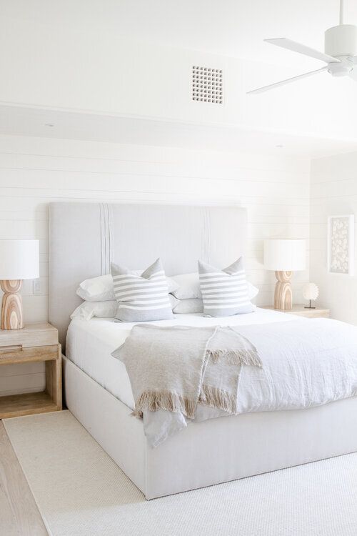a lovely neutral contemporary bedroom with planked walls, an upholstered bed with neutral bedding, matching wooden nightstands and a large fan