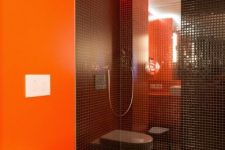 a minimalist bathroom with an orange accent wall, a shower space clad with black tiles is a very chic and cool space