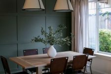 a modern dining space with a dark green paneled accent wall, a light stained table, brown leather chairs, pendant lamps and neutral curtains