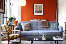 a modern living room with an orange accent wall, a grey sofa, a striped chair, a low coffee table and some bold artworks