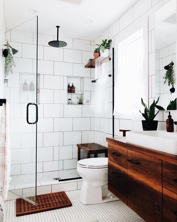 a modern white bathroom with various types of tiles, a dark stained floating vanity and a matching mat and bench, potted greenery